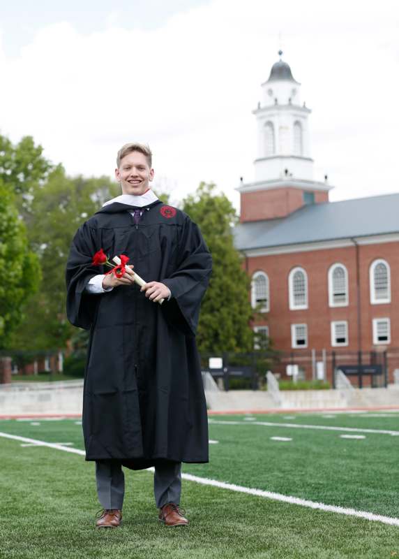 a man in a graduation gown holding flowers