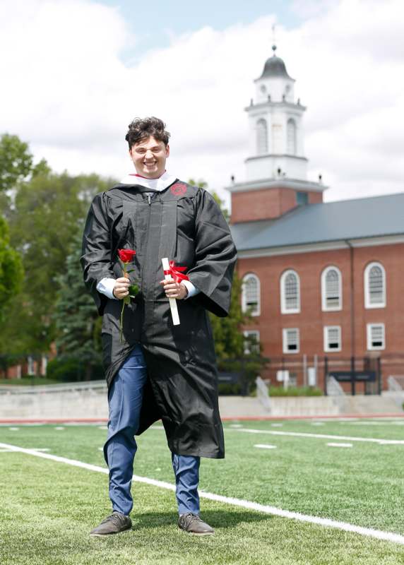 a man in a graduation gown holding a rose and a diploma