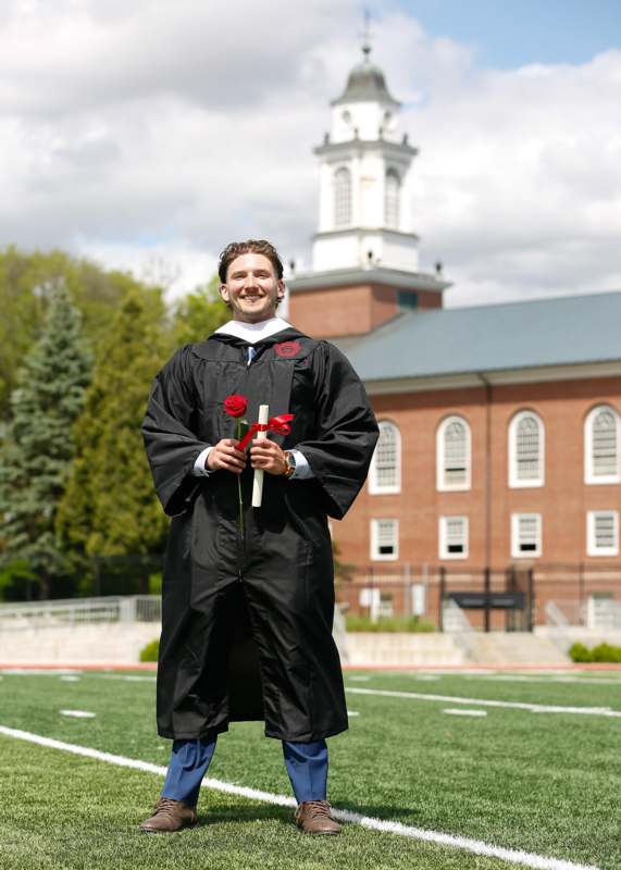 a man in a graduation gown holding a rose and a diploma