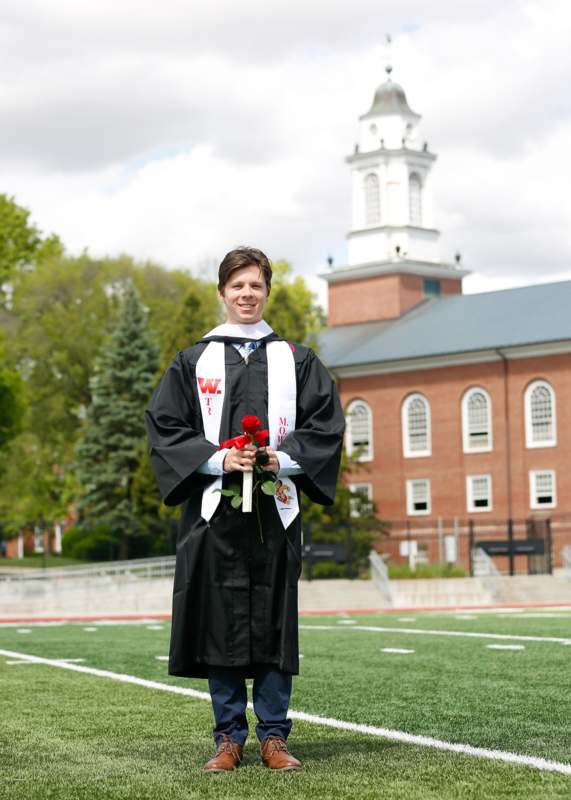 a man in a graduation gown holding flowers