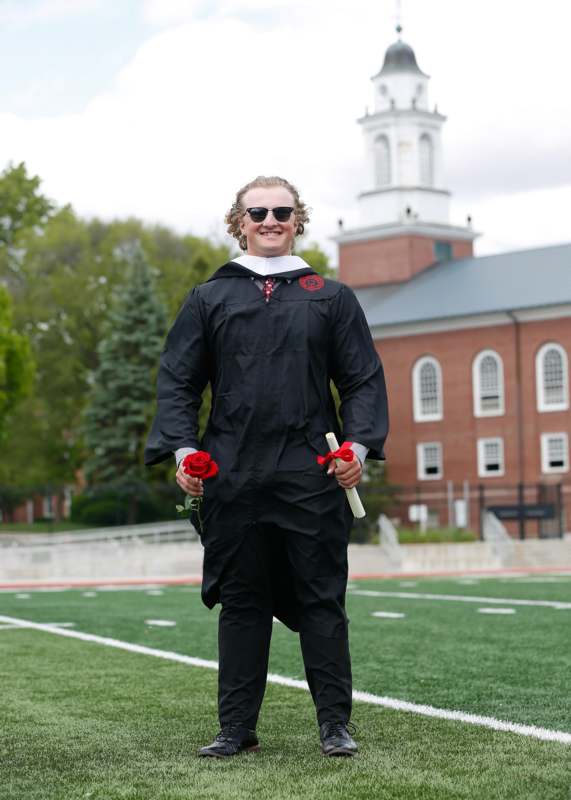 a man in a graduation gown holding a rose and diploma