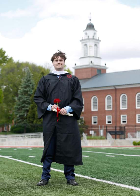 a man in a graduation gown holding a rose