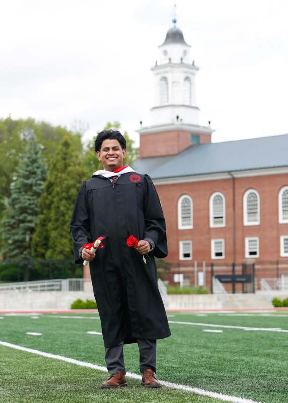 a man in a graduation gown holding roses