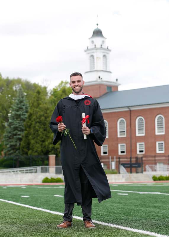 a man in a graduation gown holding a rose and a diploma