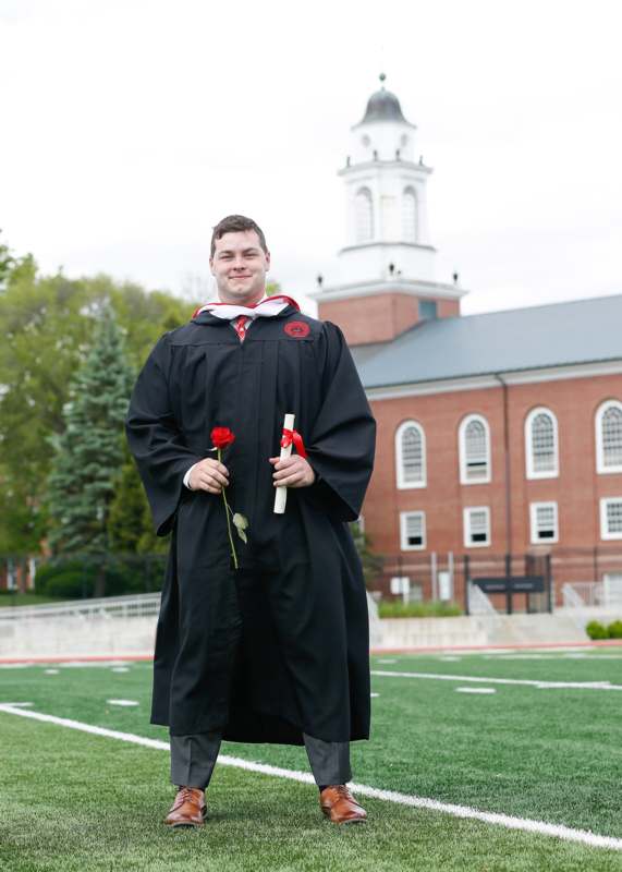 a man in a graduation gown holding a rose and a diploma