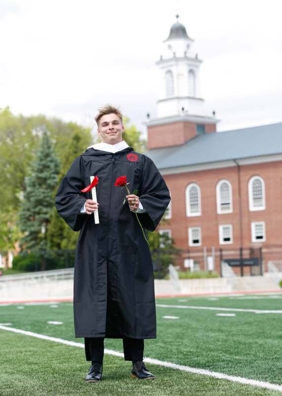 a man in a graduation gown holding a rose and a red rose
