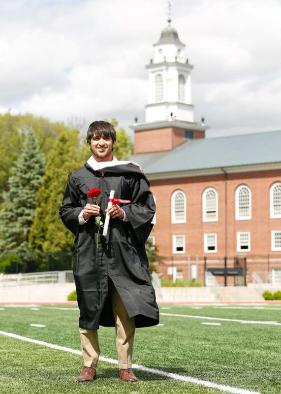 a man in a graduation gown holding a rose and a red ribbon