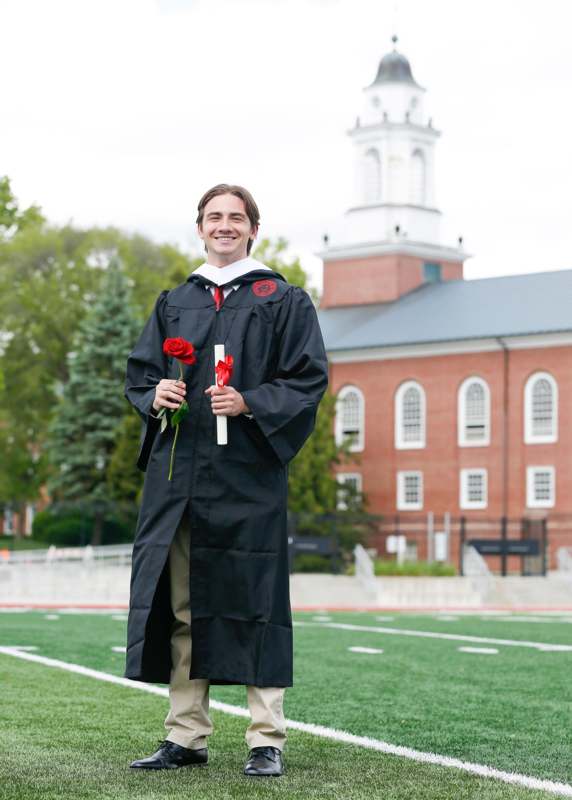 a man in a graduation gown holding a rose and standing on a football field