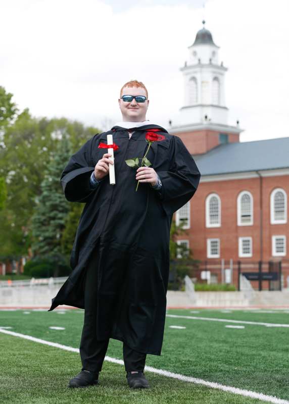 a man in a graduation gown holding a rose and a diploma