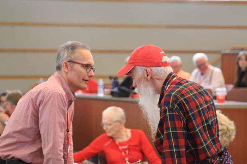 a man with a long beard and red hat talking to another man