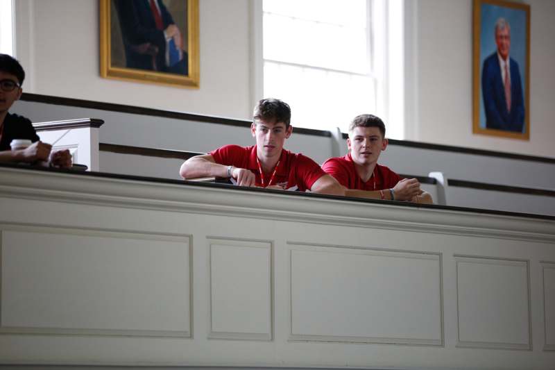 two men in red shirts sitting on a white wall