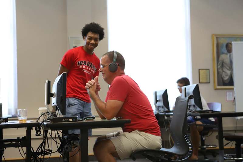 a man wearing headphones and sitting at a desk with a young boy in the background