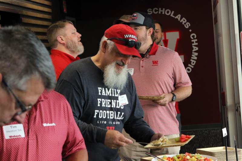 a man in a red hat and a white beard standing next to a table full of food