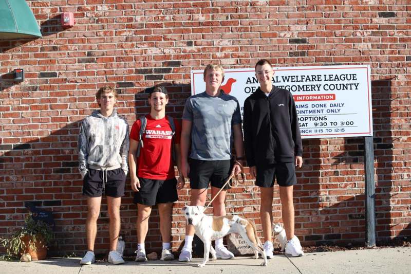 a group of men standing in front of a brick wall with a dog