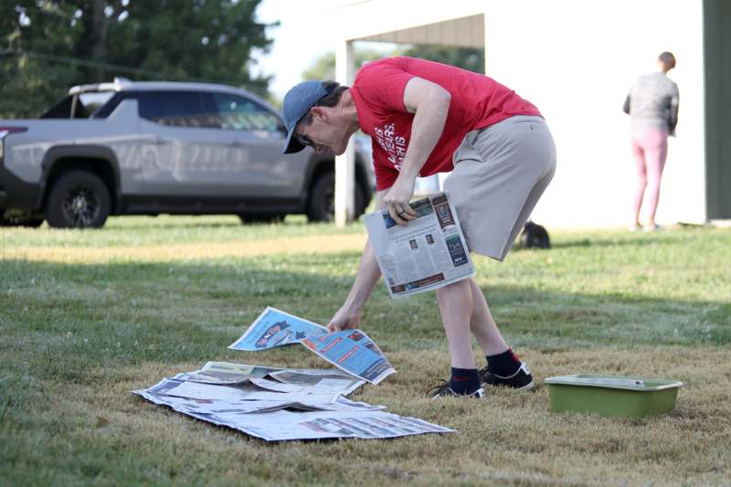 a man in a red shirt and cap looking at newspapers on the ground