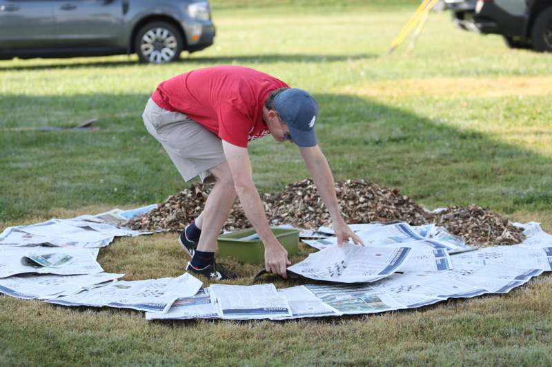 a man in a red shirt and khaki shorts kneeling on a pile of newspapers