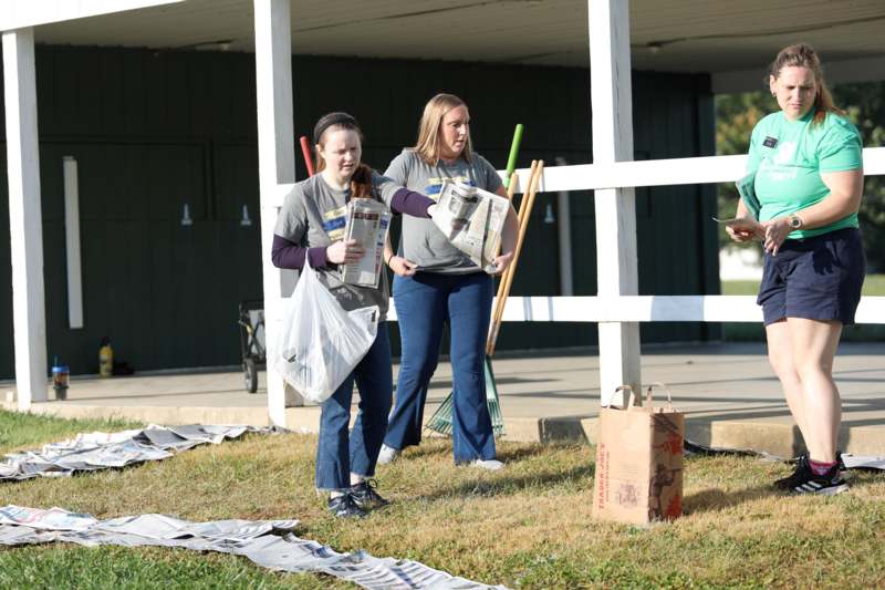 a group of women holding newspapers and a man standing on grass
