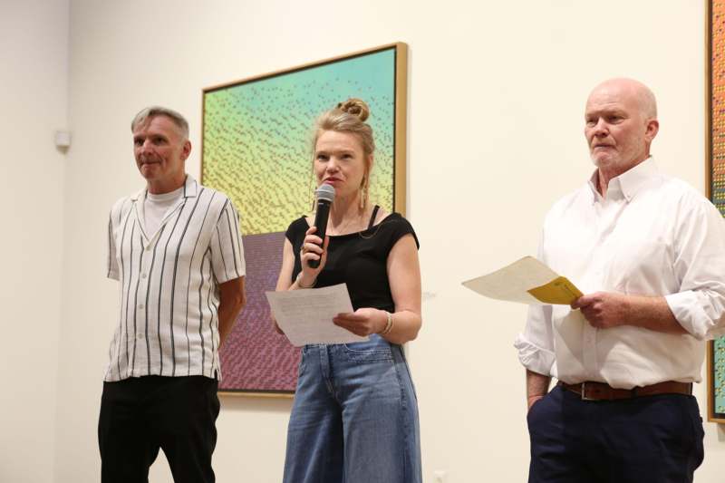 a woman holding a microphone and a man standing next to a painting