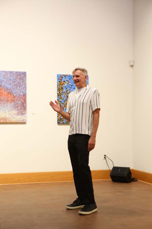 a man standing in front of a wall with paintings on the wall
