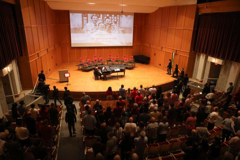 a group of people in a room with a stage and a piano