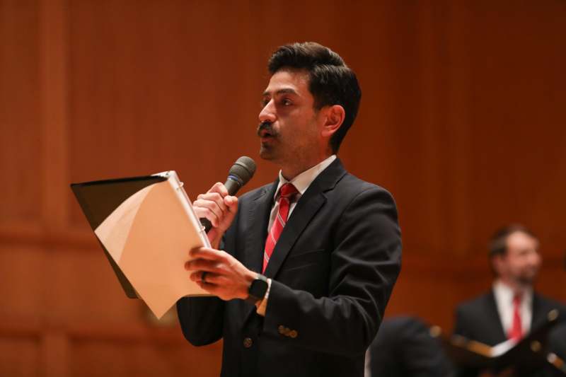 a man in a suit holding a microphone and holding a piece of paper