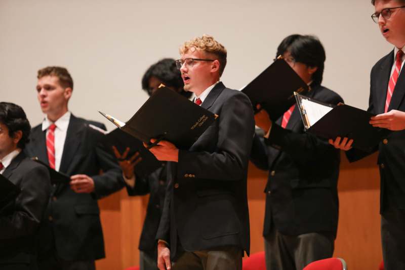 a group of men singing into folders