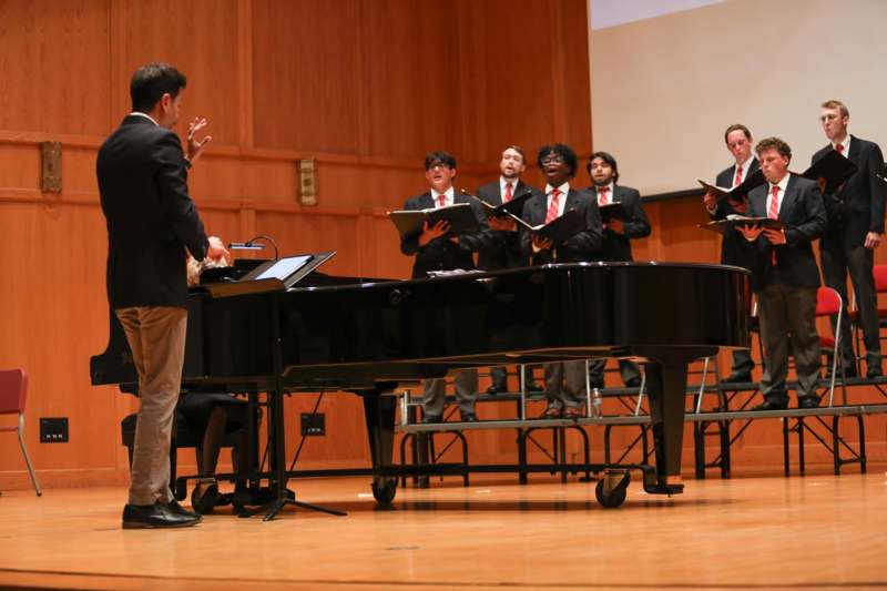 a group of men singing in front of a piano