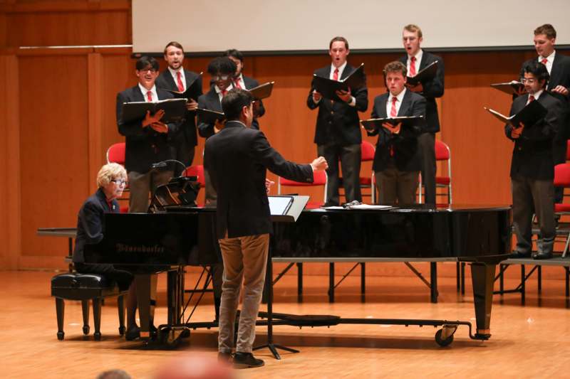 a group of men in suits and a man standing in front of a piano