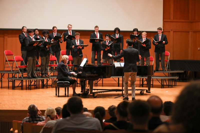a group of people on a stage with a piano and a man in front of them