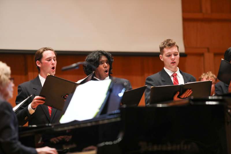 a group of people singing in front of a piano