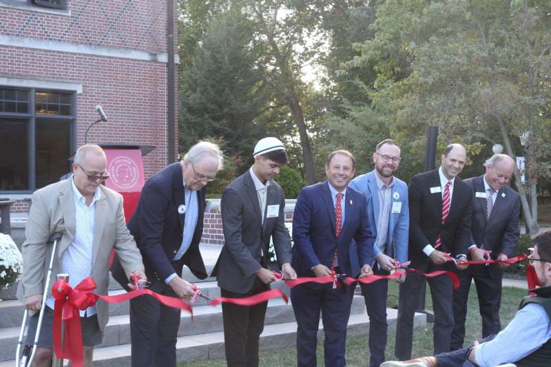 a group of men cutting a red ribbon