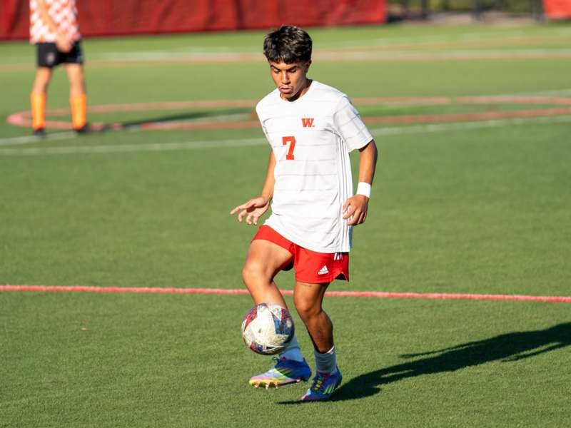 a boy in a white shirt and red shorts kicking a football ball
