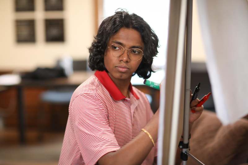 a man in glasses writing on a white board