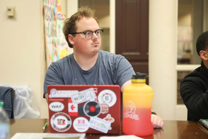 a man sitting at a table with a laptop and a bottle