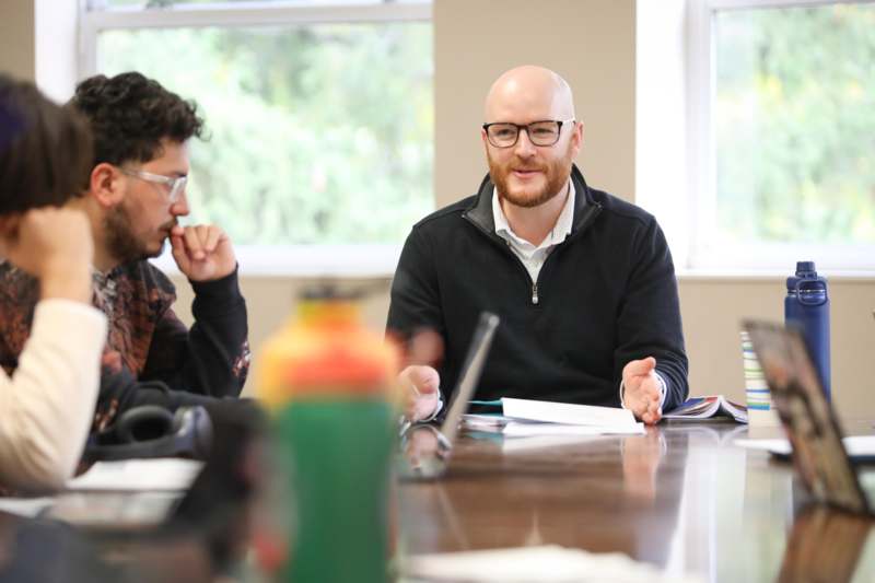 a man sitting at a table with another man in the background