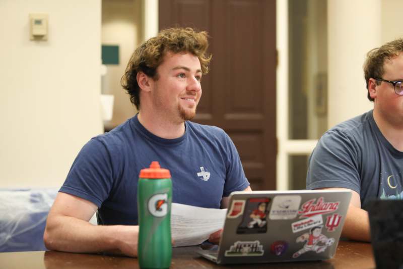 a man sitting at a table with a laptop and a bottle of water