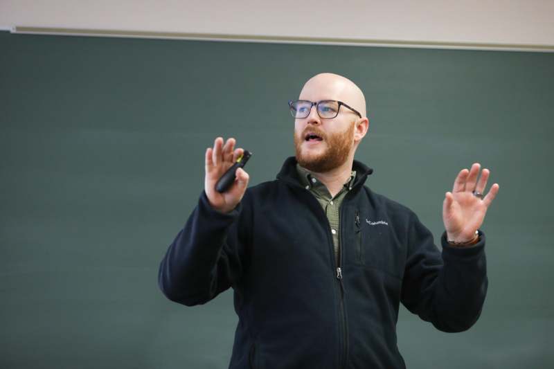 a man in glasses holding a device in front of a chalkboard
