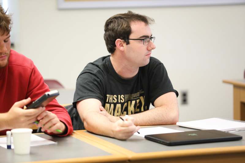 a man sitting at a table with a pen and a laptop