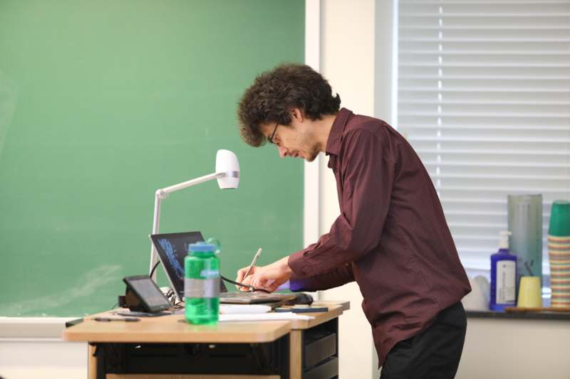 a man standing at a desk with a laptop and a lamp
