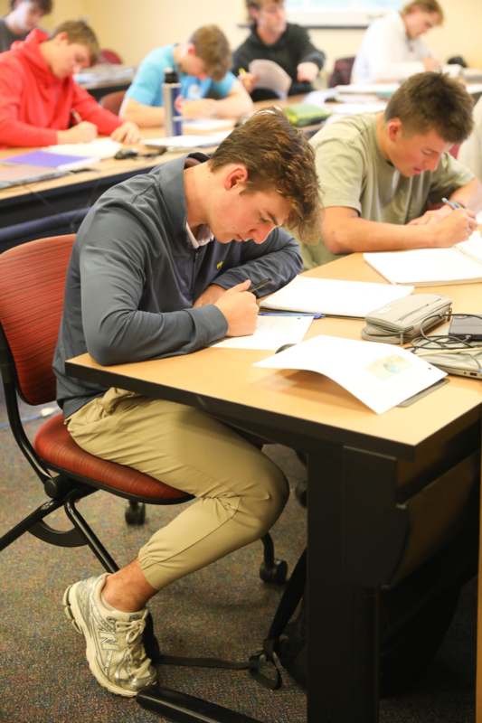 a group of people sitting at a table writing on paper