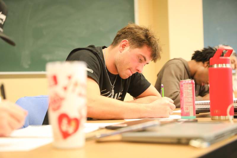 a man writing on paper in a classroom