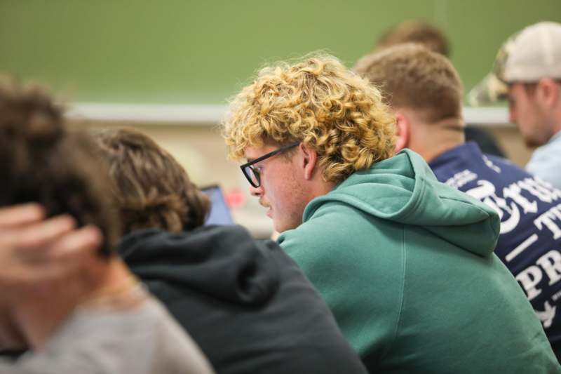 a man with curly blonde hair sitting in a classroom