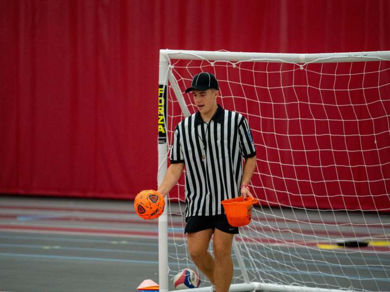 a man in a black and white striped shirt holding a ball and a orange bucket