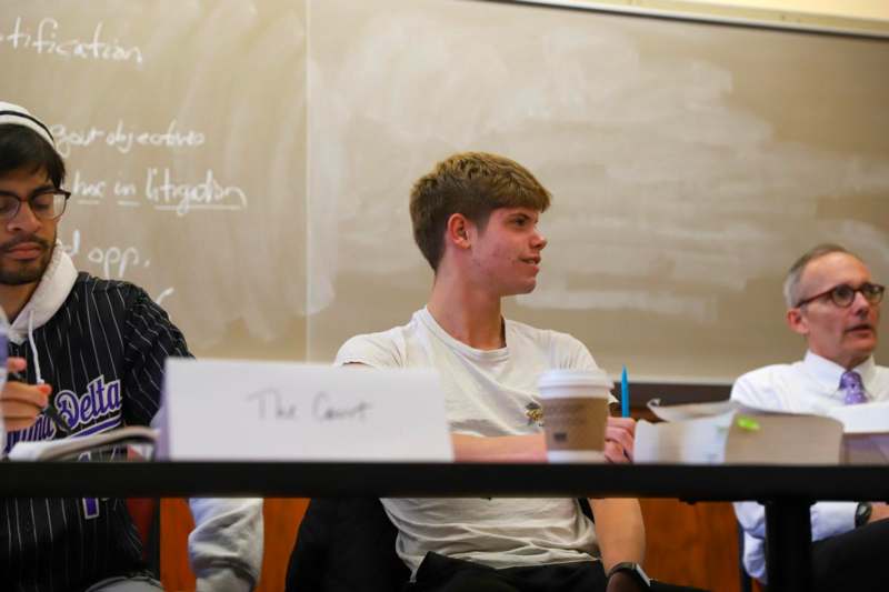 a man sitting at a table with a cup of coffee and a white board