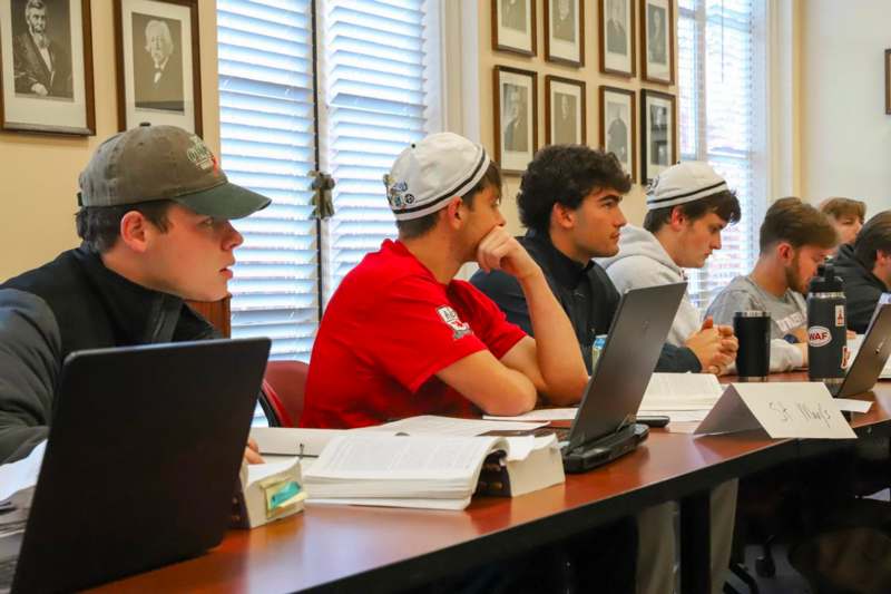 a group of people sitting at a table with laptops and books