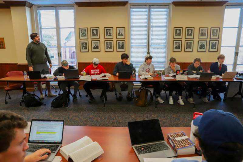 a group of people sitting at a long table with laptops