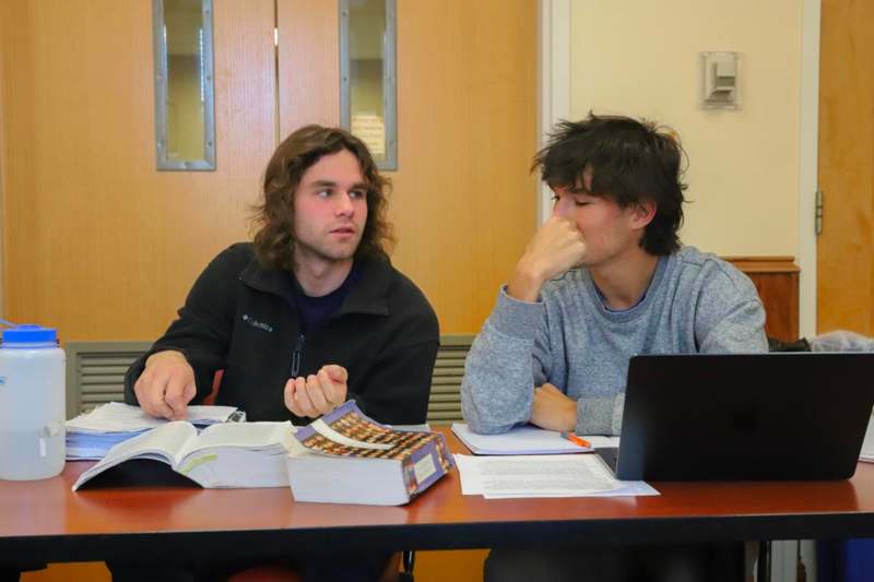 two men sitting at a table with books and a laptop