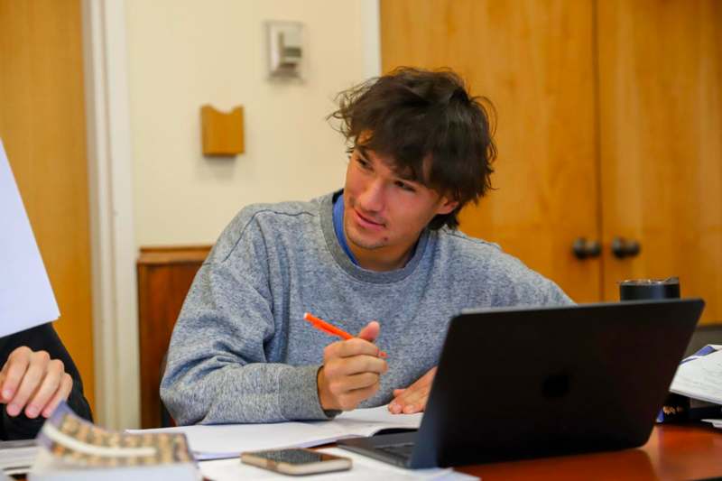 a man sitting at a desk with a laptop and a pen