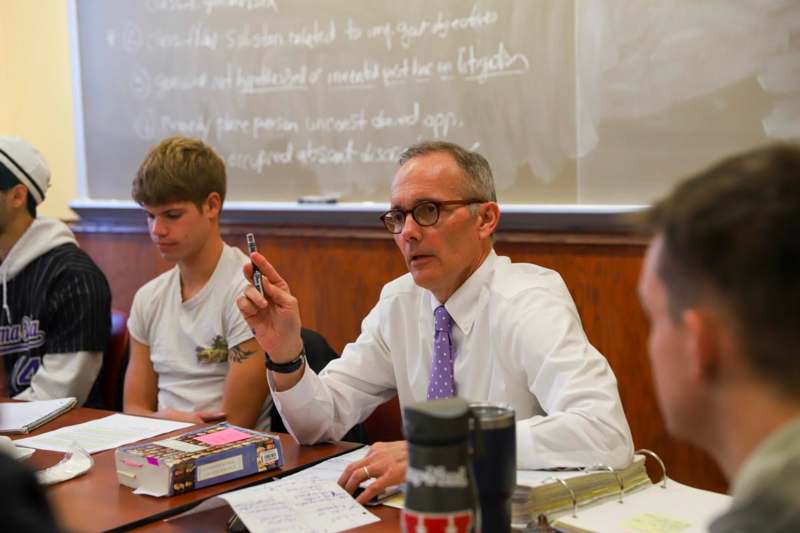 a man in a white shirt and purple tie sitting at a table with other people