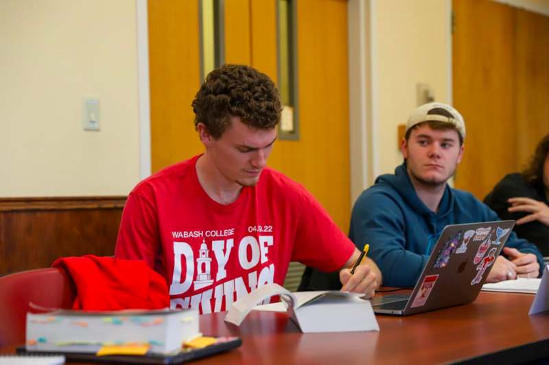a group of men sitting at a table with laptops and books